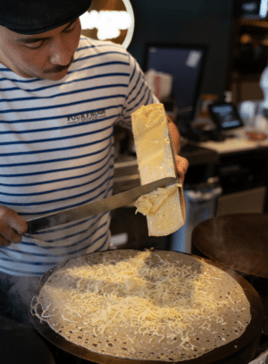 A chef scraping raclette onto a galette la tartiflette